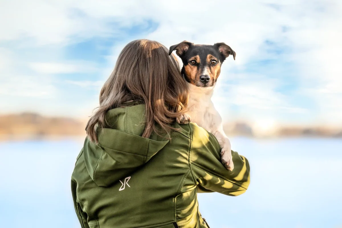 Ein kleiner Hund auf dem Arm seiner Besitzerin am See