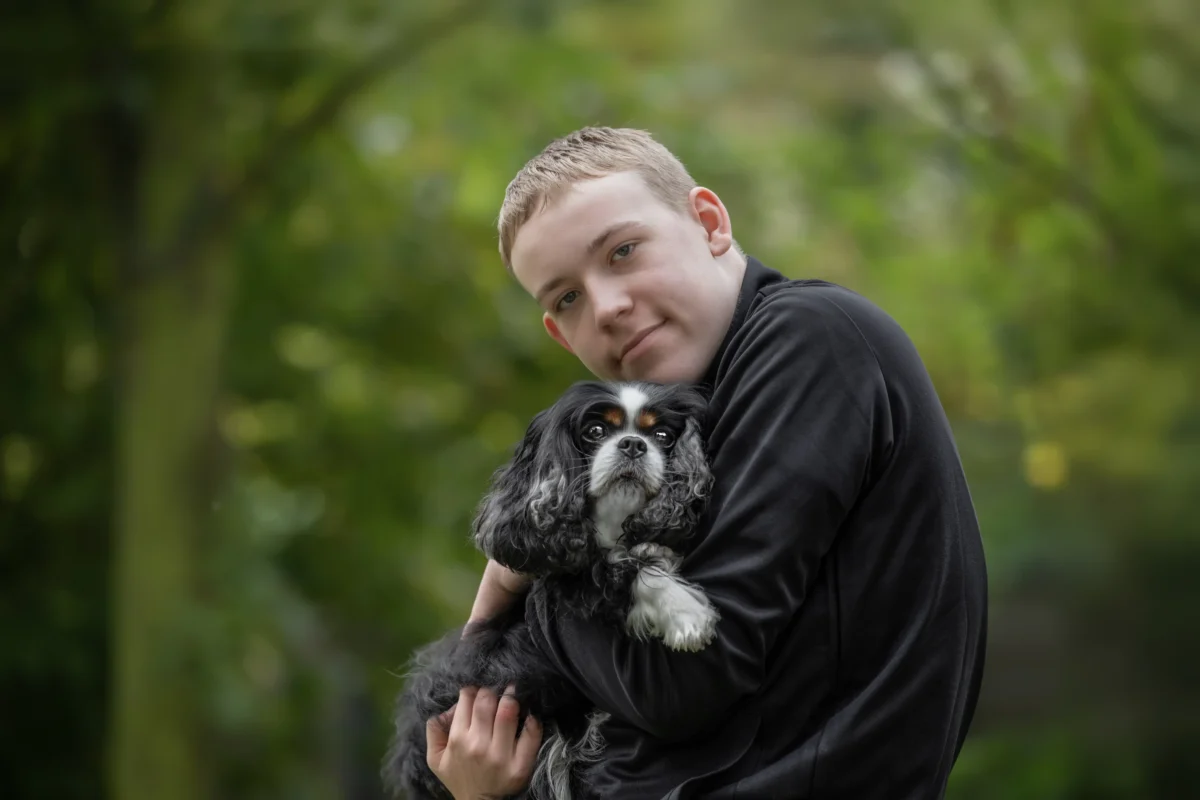Ein großer Junge hält einen kleinen Hund im Arm.