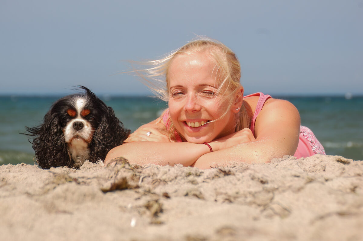 Ein Cavalier King Charles Spaniel und eine junge Frau am Strand